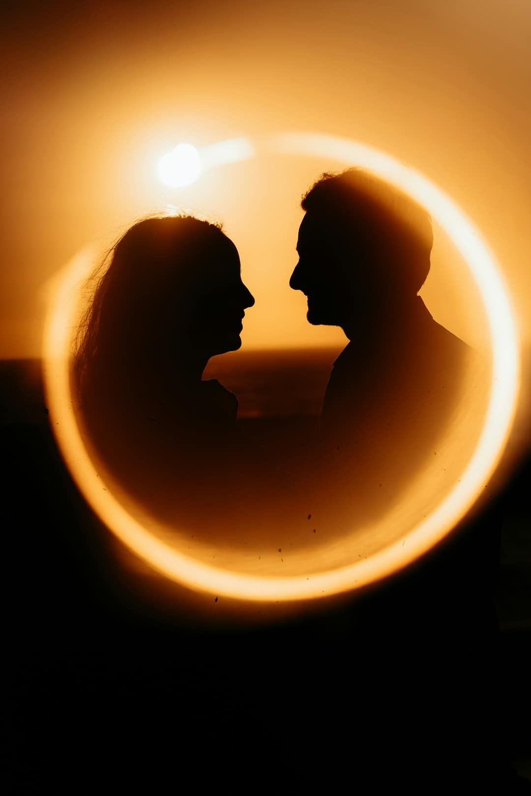 The couple in silhouette at sunset, framed by a ring of light